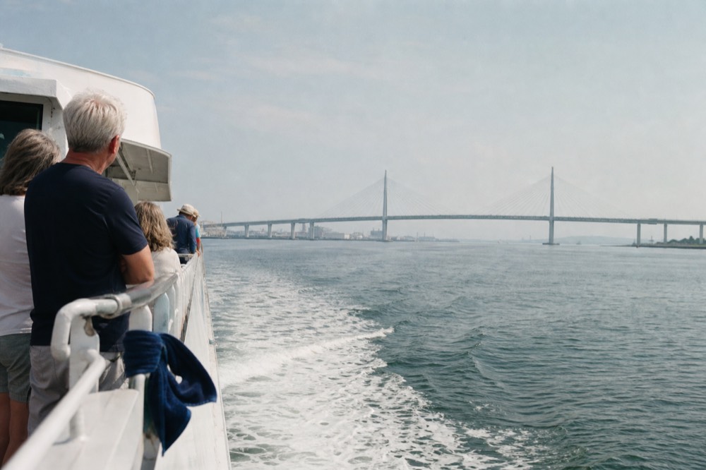 A classic excursion boat underway on calm harbor water toward a suspension bridge, no text, no logos, no people