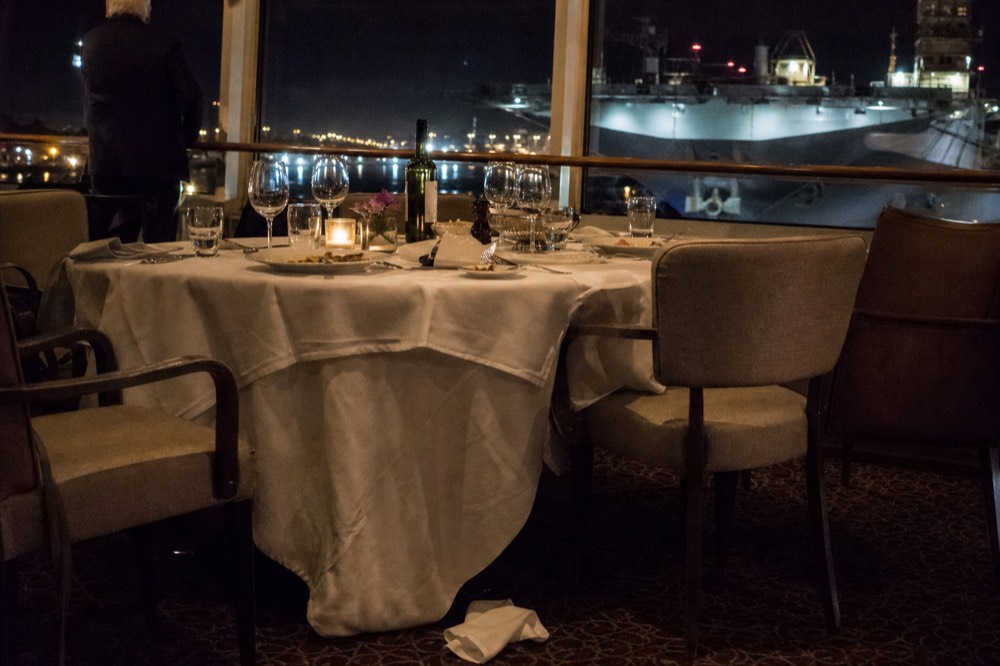 A set dinner table on a cruise boat deck with harbor lights beyond, no text, no logos, no people