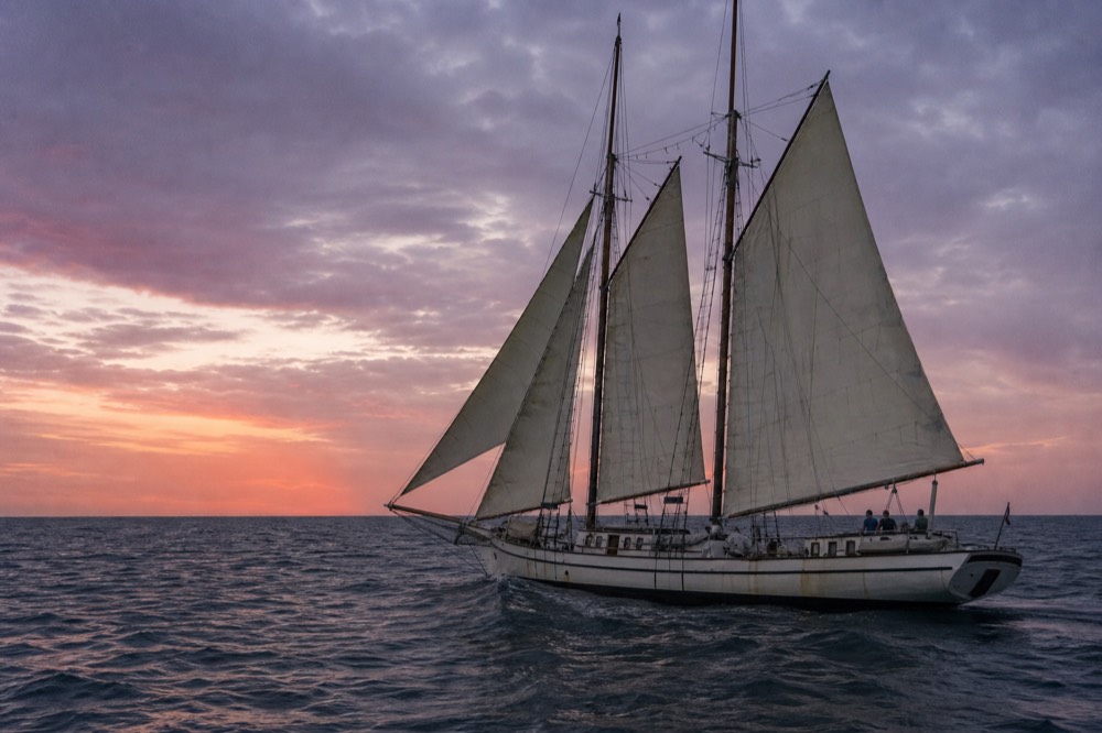 A three-masted schooner under sail on open water at dusk, no text, no logos, no people