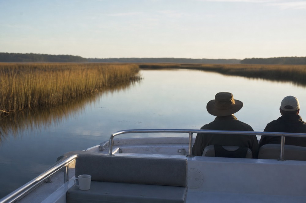 A tour boat drifting on calm morning water in a salt marsh creek, no text, no logos, no people