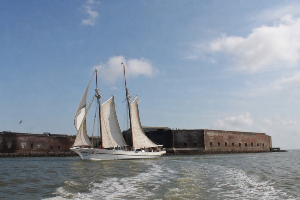 A tall ship sailing past Fort Sumter with a dolphin wake in the foreground, no text, no logos, no people