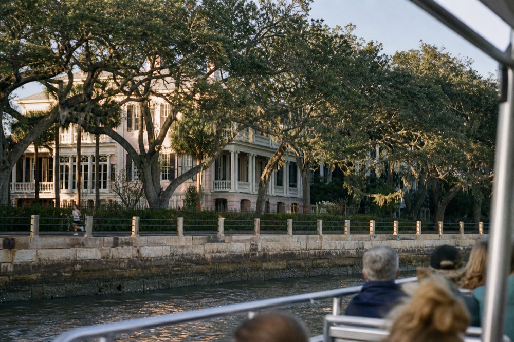 A narrated harbor tour boat passing the Battery seawall and mansions in afternoon light, no text, no logos, no people