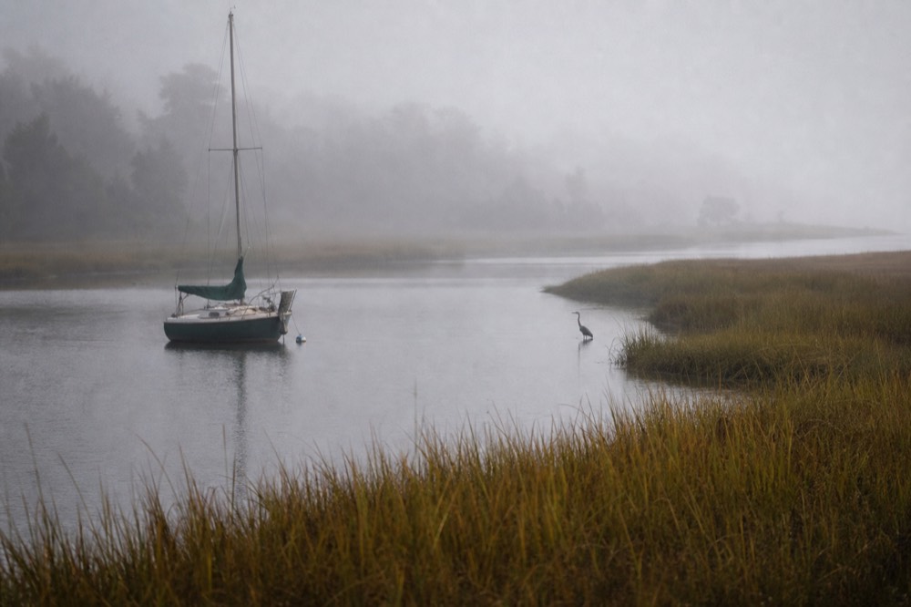 A small quiet sailing yacht anchored near a marsh creek with no other boats nearby, no text, no logos, no people