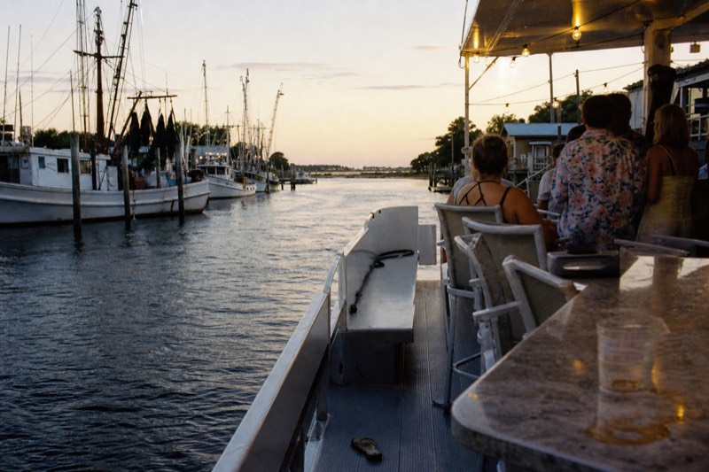 Party boat easing down Shem Creek on a warm evening with string lights switched on for a Charleston harbor social cruise