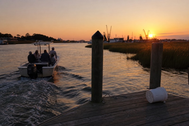 Boat pulling out of Shem Creek at sunset past silhouetted shrimp boats on a Charleston harbor cruise