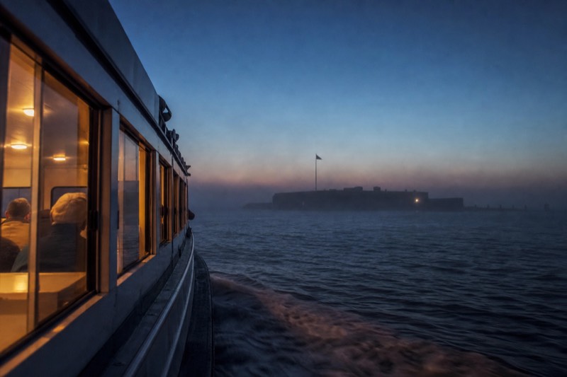 Narrated tour boat passing the dark silhouette of a Charleston harbor fort at blue hour on a haunted history cruise
