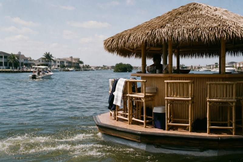 Bamboo tiki-bar boat crossing Charleston Harbor on a bright afternoon with a thatched roof shading the deck