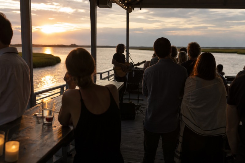 Guests on a Charleston sunset cruise with onboard music and bar, harbor water turning copper at golden hour