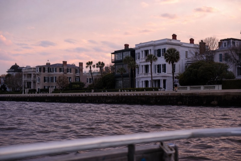 Pastel sunset sky behind Charleston Battery mansion rooftops seen from a drifting harbor cruise boat